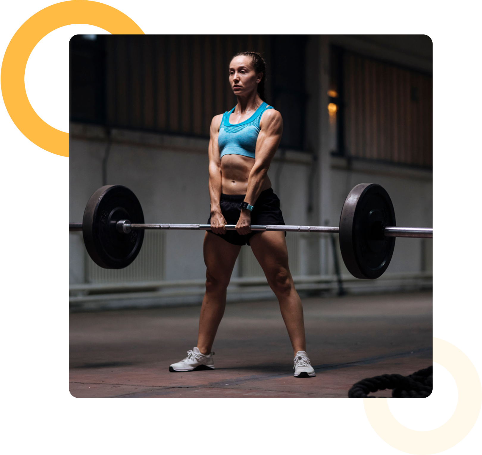 A woman in athletic wear performs a deadlift with a barbell in an indoor gym setting.