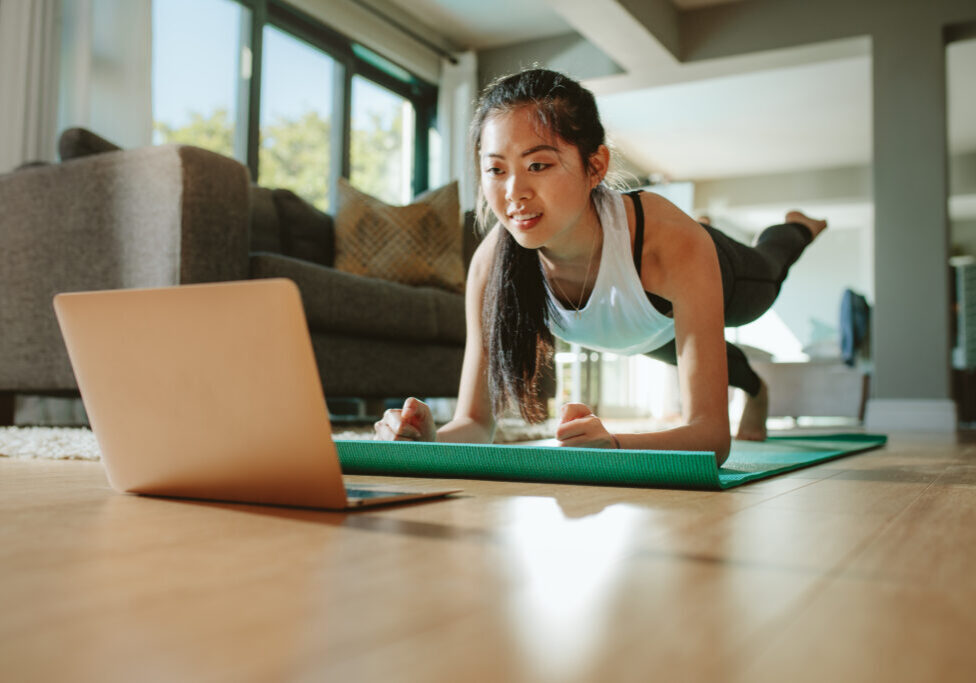 Woman working out at home watching video tutorial on laptop. Fit young woman in plank position repeating online instructions by coach on computer.
