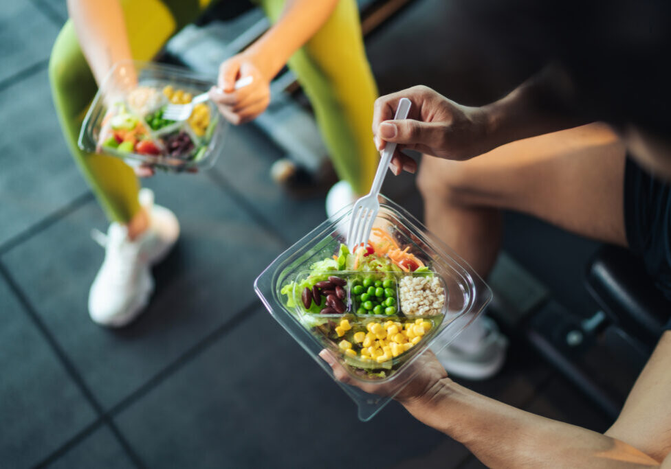 Top view Asian man and woman healthy eating salad after exercise at fitness gym. Two athlete eating salad for health together. Selective focus on salad bowl on hand.