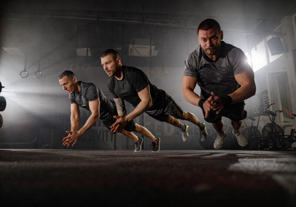 Group of young athletic men exercising push-ups while clapping their hands in a gym. Copy space.
